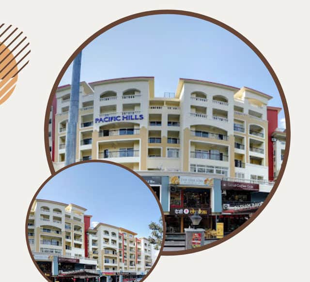 Pacific Hills community on Rajpur Road in Malsi, cream and terracotta facade with arched windows and a retail arcade at ground level.