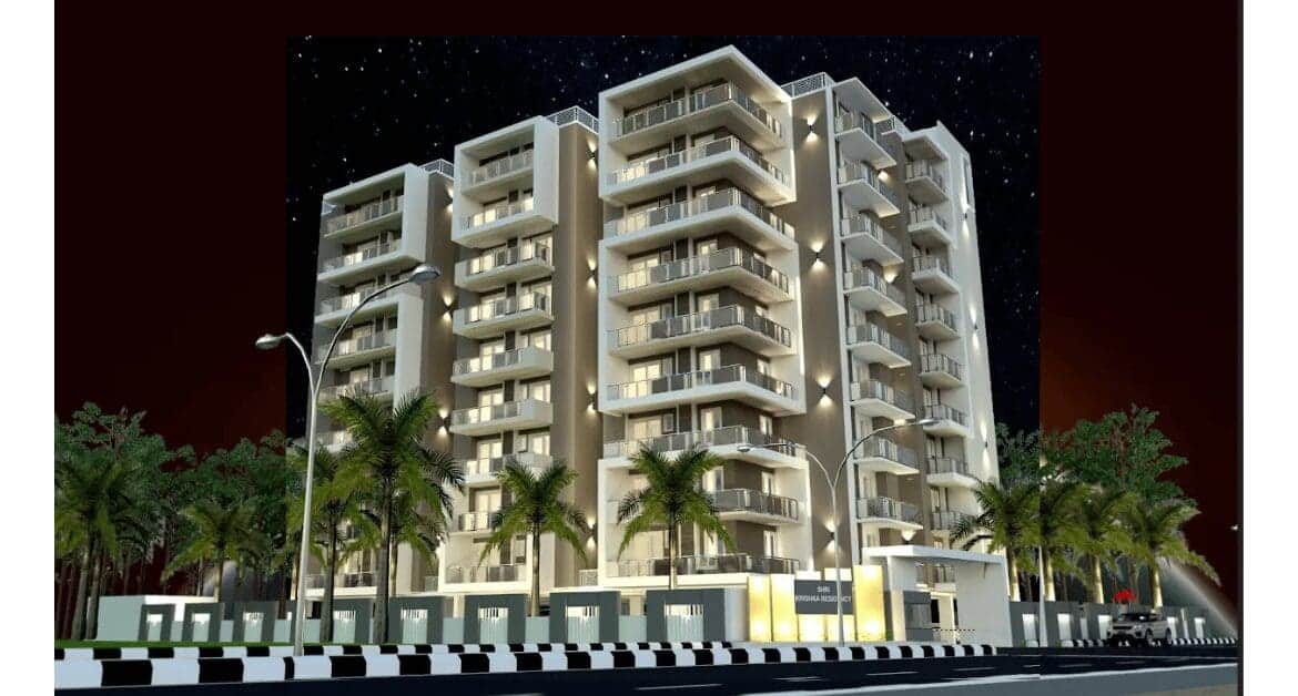 Shri Krishna Residency tower on GMS Road, lit balconies against a night sky with palms lining the boundary wall.